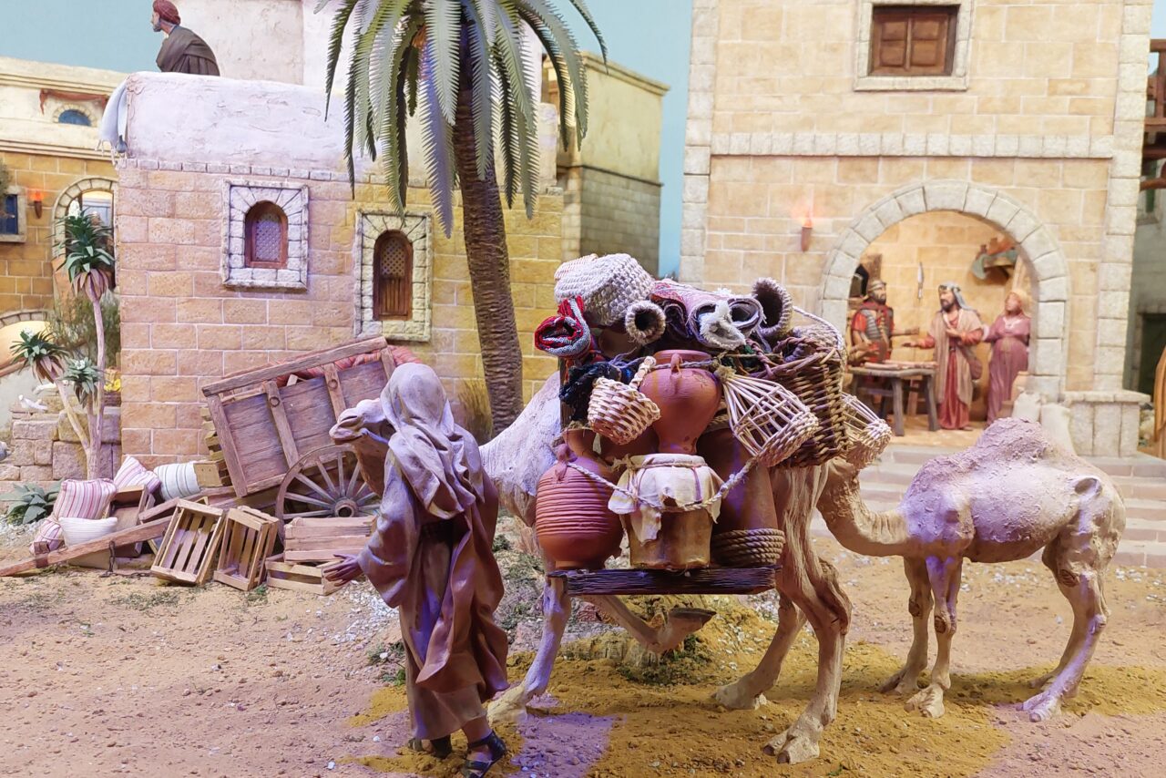 Joulupienoismalli, jossa vanhoja rakennuksia, ihmisiä, aaseja tavaroita selässään ja palmu.